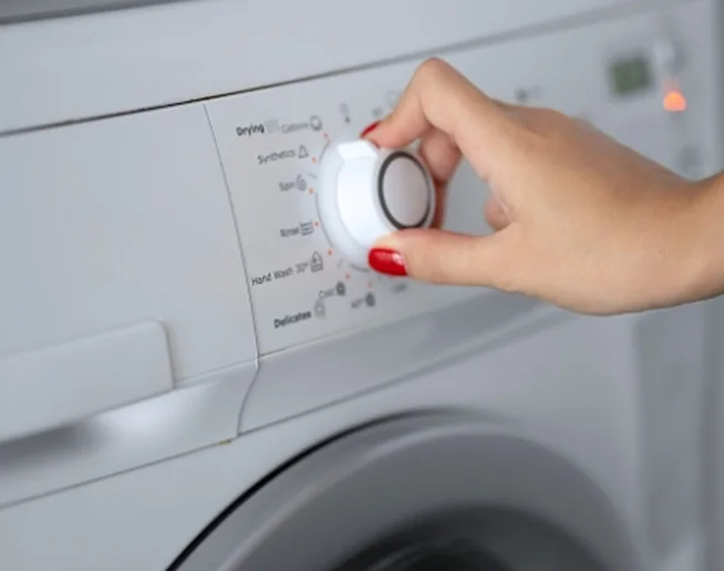 A hand turning the cycle dial on a washing machine